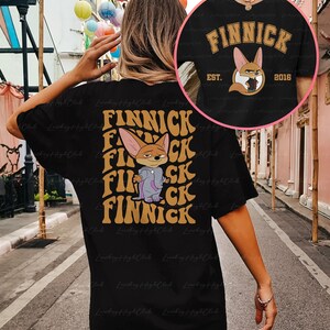 May include: Black t-shirt with a graphic print of a cartoon fox wearing a purple jacket and the text "FINNICK" in a retro font. The text "EST. 2016" is also printed on the shirt.
