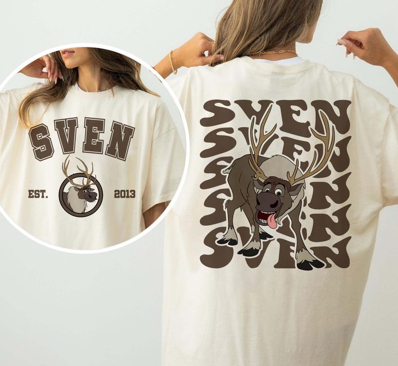Pode incluir: Camiseta creme com um gr&aacute;fico marrom de Sven, a rena do filme Frozen. A frente da camiseta tem o nome "SVEN" acima de um emblema circular com Sven e o texto "EST. 2013". A parte de tr&aacute;s da camiseta repete "SVEN" em um padr&atilde;o ondulado.