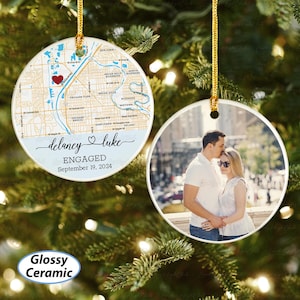 May include: Glossy ceramic Christmas ornament. One ornament features a map with a red heart, the names "delaney & luke", and the text "ENGAGED September 19, 2024". The other ornament has a photo of a couple.