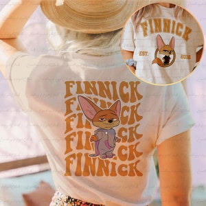 May include: White t-shirt with a cartoon fox wearing a purple hooded sweatshirt and the text "FINNICK" repeated in a retro font.