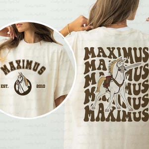 May include: Cream-colored t-shirt featuring the word "MAXIMUS" in brown, with a horse graphic. The front of the shirt has the word "MAXIMUS" and a horse graphic inside a circle, with "EST. 2010". The back of the shirt has the word "MAXIMUS" repeated with a horse graphic.