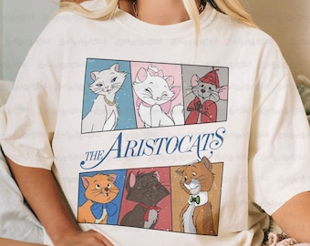 May include: Cream-colored t-shirt featuring a graphic of characters from Disney's "The Aristocats." The design includes six cartoon images of cats and a mouse, with the film's title in blue script. The shirt has a relaxed fit.