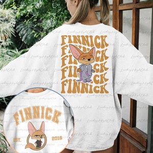 May include: A white sweatshirt with a cartoon fox wearing a purple robe and the word "FINNICK" repeated in a retro font. The sweatshirt also has a smaller image of the fox with the text "FINNICK EST. 2016" on the front.