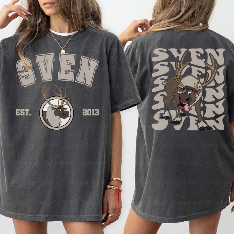 Pode incluir: Camiseta cinza escuro com o nome "SVEN" em um design de letras em bloco na frente e nas costas. A frente apresenta um gr&aacute;fico de rena e o texto "EST. 2013". As costas t&ecirc;m um gr&aacute;fico de rena e o nome "SVEN" repetido.
