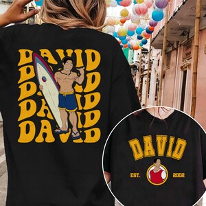 a woman wearing a black shirt with a picture of a man holding a surfboard