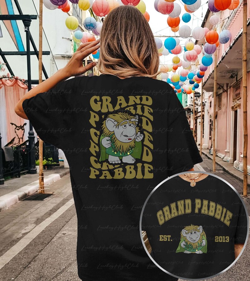May include: Black t-shirt with a graphic print of a cartoon character with the text "Grand Pabbie" in yellow letters. The character is wearing a green robe and has a white beard. The text "Grand Pabbie" is also printed on a black t-shirt with a white border.