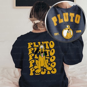 May include: A navy blue sweatshirt with a yellow graphic of Pluto the dog. The graphic features the text "PLUTO" repeated in a circular pattern around Pluto. The back of the sweatshirt has the text "PLUTO EST. 1928" in yellow.