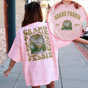 May include: Pink oversized t-shirt with a graphic of a green troll with a gold crown and the text "GRAND PABBIE" in a retro font. The text "EST. 2013" is also on the shirt.