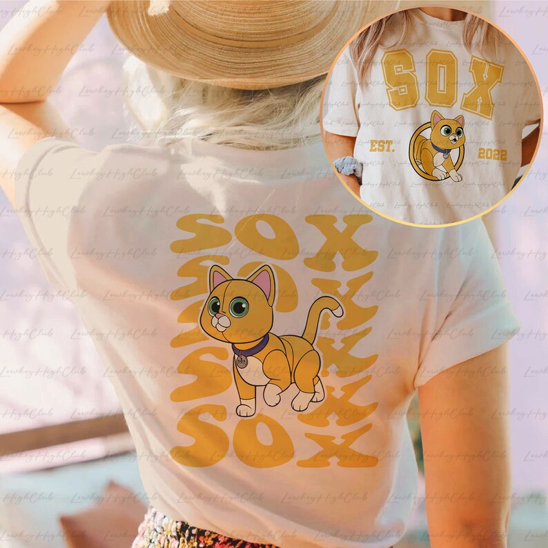 May include: White t-shirt with a yellow graphic of a cat and the text "SOX" repeated multiple times. The cat is wearing a collar with a tag. The text "EST. 2022" is also visible on the shirt.