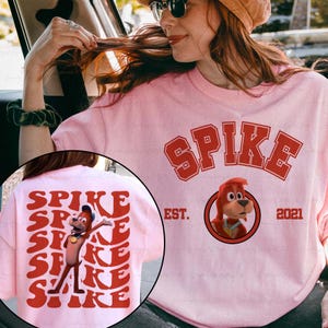 May include: Pink t-shirt with the word "SPIKE" in red block letters. The shirt features a cartoon dog graphic and the text "EST. 2021". The back of the shirt has the word "SPIKE" repeated in a stacked design.