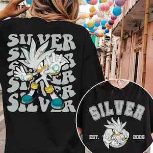 May include: Black t-shirt featuring a graphic of Silver the Hedgehog with the word "SILVER" repeated in a stacked design. A smaller circular graphic shows Silver and the text "SILVER" with "EST. 2006".