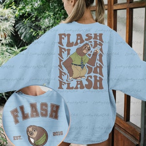 Puede incluir: Sudadera azul claro con un gr&aacute;fico de perezoso marr&oacute;n y el texto "FLASH" en una fuente retro. El perezoso lleva una camisa verde y una corbata. La sudadera tambi&eacute;n tiene el texto "FLASH" en una fuente colegial marr&oacute;n con el texto "EST. 2016" debajo.