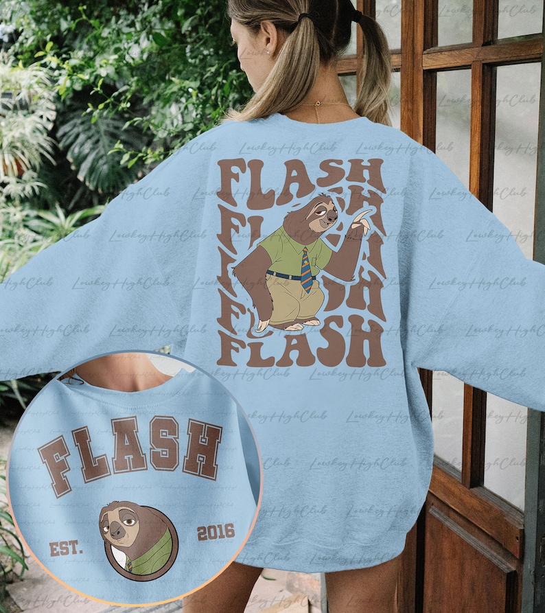 Puede incluir: Sudadera azul claro con un gr&aacute;fico de perezoso marr&oacute;n y el texto "FLASH" en una fuente retro. El perezoso lleva una camisa verde y una corbata. La sudadera tambi&eacute;n tiene el texto "FLASH" en una fuente colegial marr&oacute;n con el texto "EST. 2016" debajo.