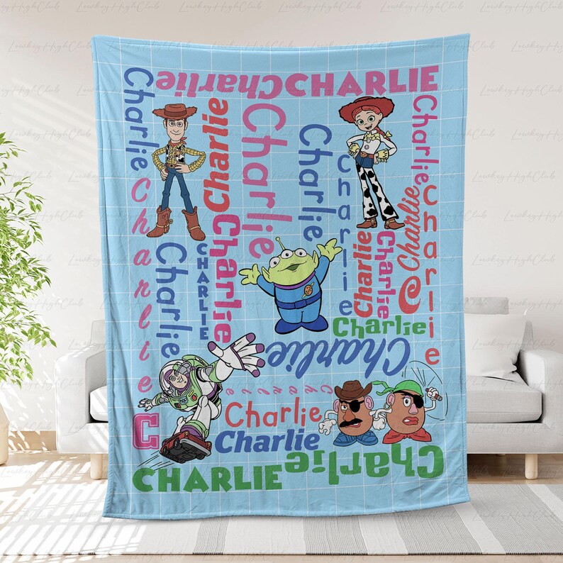 May include: A light blue fleece blanket featuring a white grid pattern and the name Charlie repeated in various colors and fonts. The design includes Toy Story characters Woody, Jessie, an alien, Buzz Lightyear, and Mr. Potato Head.