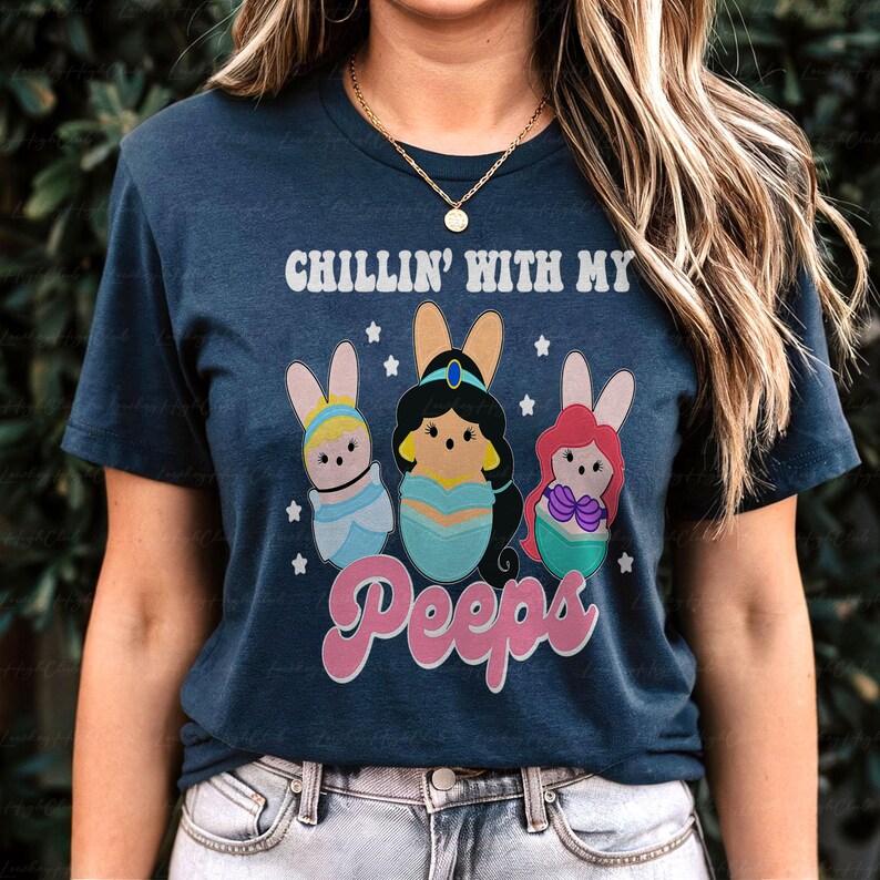 May include: Navy blue t-shirt with the text "CHILLIN' WITH MY Peeps". The shirt features a graphic of three cartoon characters dressed as Easter bunnies. The characters are in pastel colors with bunny ears.