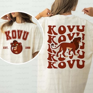 May include: Cream-colored t-shirt featuring the word "KOVU" in a maroon collegiate font, with a lion graphic and the text "EST. 1998." The back of the shirt displays the word "KOVU" in a repeating pattern with a lion graphic.