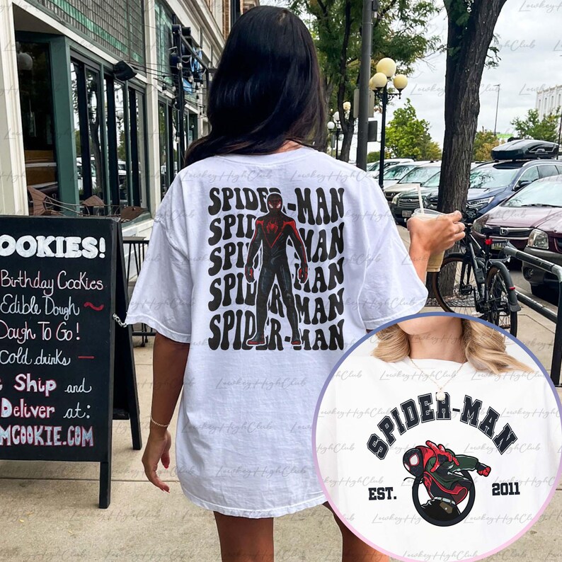May include: White t-shirt with a black and red Spider-Man graphic on the back. The graphic features the text "SPIDER-MAN" repeated in a retro style. The front of the shirt features a smaller Spider-Man graphic with the text "SPIDER-MAN EST. 2011".