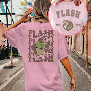 Puede incluir: Camiseta rosa con un gr&aacute;fico de perezoso marr&oacute;n y el texto "FLASH" repetido en un patr&oacute;n ondulado. El perezoso lleva una camisa verde y una corbata. El texto "EST. 2016" tambi&eacute;n est&aacute; en la camiseta.