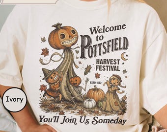 May include: An ivory t-shirt featuring a graphic print with the text Welcome to POTTSFIELD HARVEST FESTIVAL ESTD 1502 You'll Join Us Someday. The illustration depicts pumpkin-headed figures, a skeleton, and a scarecrow amidst autumn leaves.