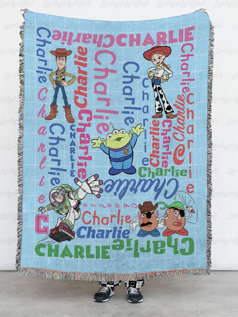 May include: A light blue woven throw blanket featuring the name Charlie repeated in various colors and fonts, alongside illustrations of Toy Story characters including Woody, Jessie, Buzz Lightyear, an alien, and two Mr. Potato Head figures.