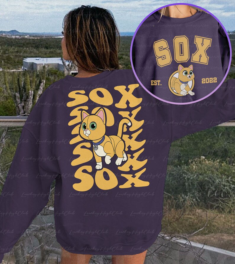 May include: Purple sweatshirt with a yellow and orange graphic of a cat with the word "SOX" repeated multiple times. The cat is wearing a collar with a tag. The text "EST. 2022" is also on the sweatshirt.