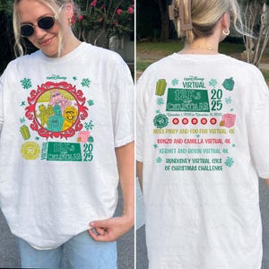May include: White t-shirt featuring a colorful Muppets design within a red and gold frame, with text that reads "12Ks of Christmas 2025." The back of the shirt lists virtual race details. The shirt has a round neck and short sleeves.
