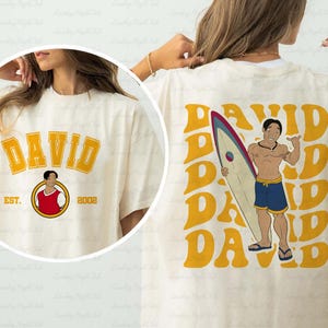 a woman wearing a t - shirt with a picture of a man holding a surf