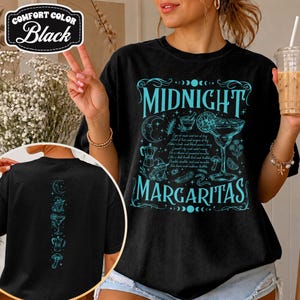 May include: A black t-shirt featuring a large turquoise graphic on the front with the text "MIDNIGHT MARGARITAS" and illustrations of a margarita glass, a frog, a crescent moon, and a moka pot. The back of the shirt displays a vertical design.