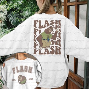 Puede incluir: Sudadera blanca con un gr&aacute;fico de perezoso marr&oacute;n y el texto "FLASH" en una fuente retro. El perezoso lleva una camisa verde y una corbata. La sudadera tambi&eacute;n tiene un gr&aacute;fico m&aacute;s peque&ntilde;o en la parte delantera con el texto "FLASH" y el a&ntilde;o "2016".