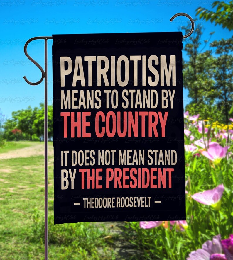 Puede incluir: Una bandera de jard&iacute;n negra con la cita "PATRIOTISMO SIGNIFICA APOYAR AL PA&Iacute;S, NO SIGNIFICA APOYAR AL PRESIDENTE - THEODORE ROOSEVELT -" en letras blancas y rojas. La bandera est&aacute; colgada de un poste de metal.