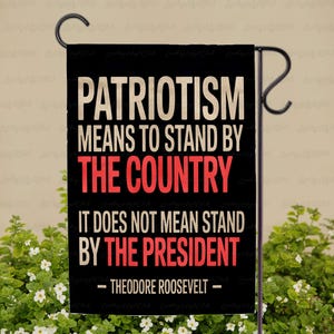 May include: Black garden flag with white and red text. The text reads: "PATRIOTISM MEANS TO STAND BY THE COUNTRY IT DOES NOT MEAN STAND BY THE PRESIDENT - THEODORE ROOSEVELT -" The flag is hanging on a black metal stand.