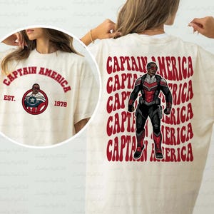 May include: Cream-colored t-shirt featuring Captain America graphics. The front displays "CAPTAIN AMERICA" in red arched text, with a circular emblem and "EST. 1978." The back showcases a Captain America figure with red text.