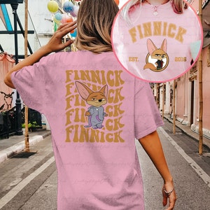 May include: Pink t-shirt with a cartoon fox wearing a purple jacket and the text "Finnick" repeated in a retro font. The text "Est. 2016" is also on the shirt.