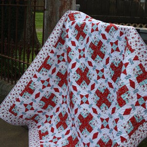 May include: A red, white, and blue patchwork quilt with a floral pattern. The quilt is folded and draped over a wooden post.