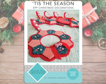 May include: A set of red and green Christmas ornaments made with English paper piecing. The ornaments are in the shape of stars, a wreath, and a bell. The ornaments are on a wooden surface. 'Tis the Season EPP Christmas Decorations by Sharon Burgess.