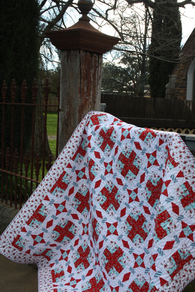 May include: A red, white, and blue patchwork quilt with a floral pattern. The quilt is folded and draped over a wooden post.