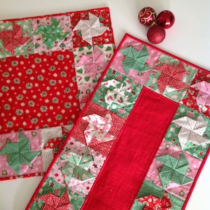 May include: Two red and white Christmas table runners with a red background and a pattern of green and pink pinwheels.