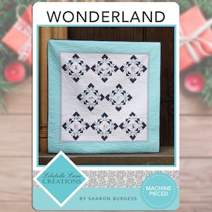 May include: A quilt pattern titled "Wonderland" by Lilabelle Lane Creations. The quilt is machine pieced and features a blue and white design with a teal border. The quilt is displayed against a wooden background.