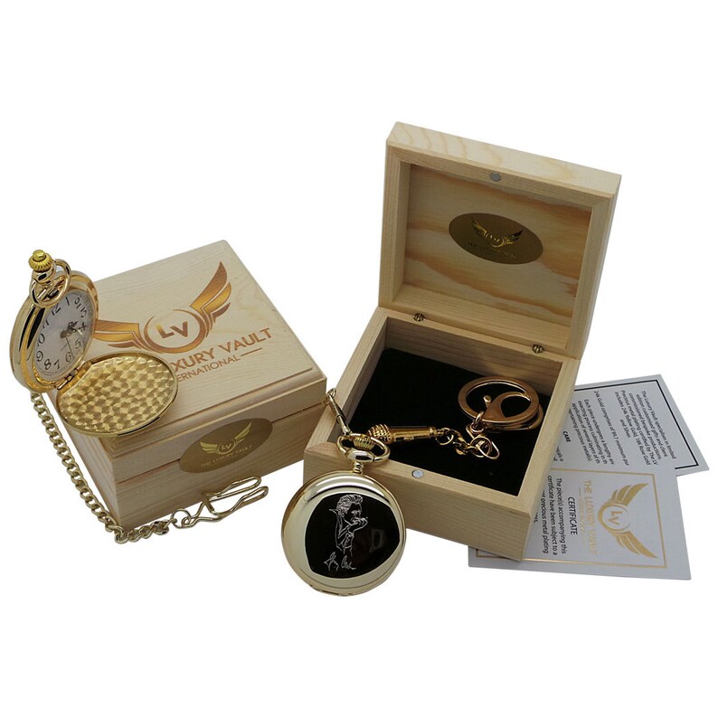 May include: A gold pocket watch with a chain and a black and white image of a man on the face. The watch is in a wooden box with a gold logo that says "Luxury Vault International".
