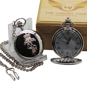 May include: Silver pocket watch with a white face and Roman numeral hour markers. The watch has a silver chain and is in a wooden box with the text "The Luxury Vault - International".