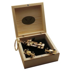 May include: A wooden box with a black velvet interior contains three gold-colored miniature race cars. One car is attached to a key chain. The box has a logo that reads "The Luxury Key".
