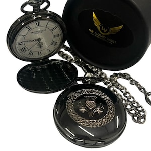 May include: Black pocket watch with a silver face and Roman numeral hour markers. The watch has a chain and a separate black pocket watch cover with a silver thistle design.