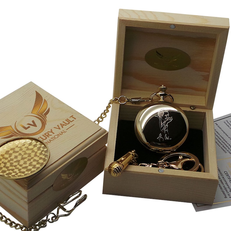 May include: Gold pocket watch with a microphone charm, engraved with a person singing, in a wooden box with a gold logo that says "Luxury Vault National".