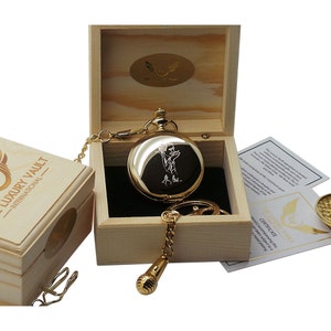 May include: A gold pocket watch with a chain and a microphone charm, engraved with a portrait of a person, comes in a wooden box with a certificate of authenticity. The box is labeled "Luxury Vault - International".
