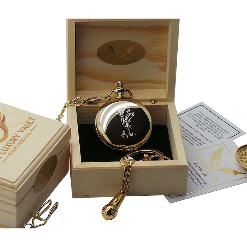 May include: A gold pocket watch with a chain and a microphone charm, engraved with a portrait of a person, comes in a wooden box with a certificate of authenticity. The box is labeled "Luxury Vault - International".