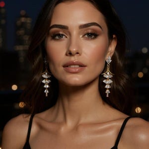 May include: A pair of gold-toned drop earrings featuring a tiered, fan-shaped design. Each earring consists of three stacked, clear, baguette-cut crystals arranged in a cascading pattern, suspended from a small, triangular crystal stud top.
