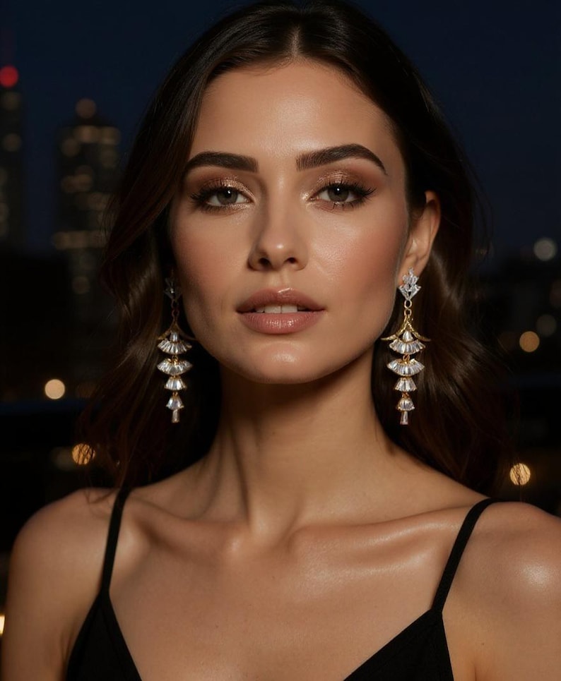 May include: A pair of gold-toned drop earrings featuring a tiered, fan-shaped design. Each earring consists of three stacked, clear, baguette-cut crystals arranged in a cascading pattern, suspended from a small, triangular crystal stud top.