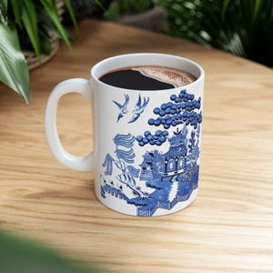 May include: White ceramic coffee mug with a blue and white willow pattern. The mug is filled with coffee and has a handle.