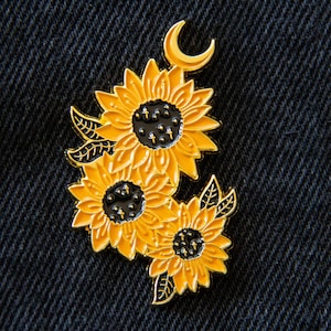 May include: Gold-tone enamel pin featuring three stylized sunflowers with black centers and a crescent moon.