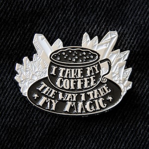 May include: Black and silver enamel pin featuring a coffee cup design with the text "I take my coffee the way I take my magic." The pin is surrounded by crystal-like shapes, perfect for a witchy aesthetic.